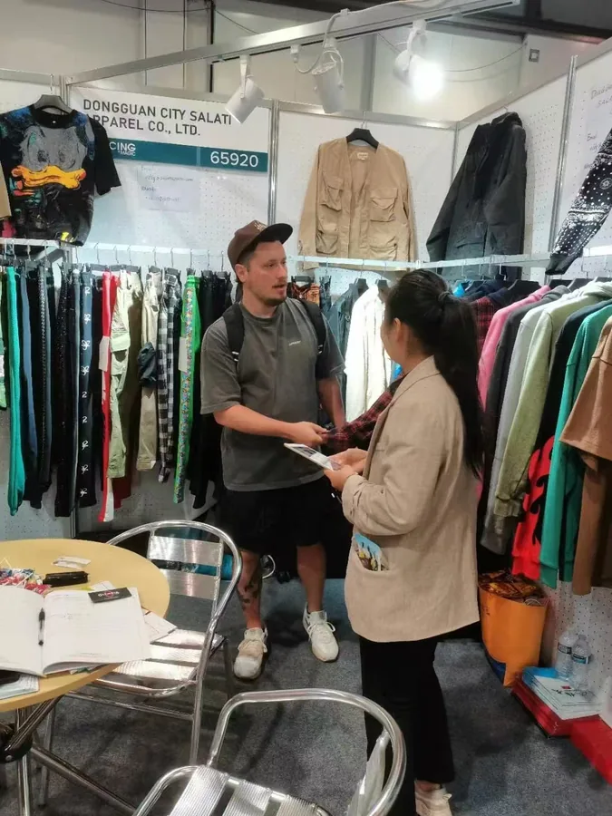 A visitor and a SALATI team member discussing garments beside the exhibition rack
