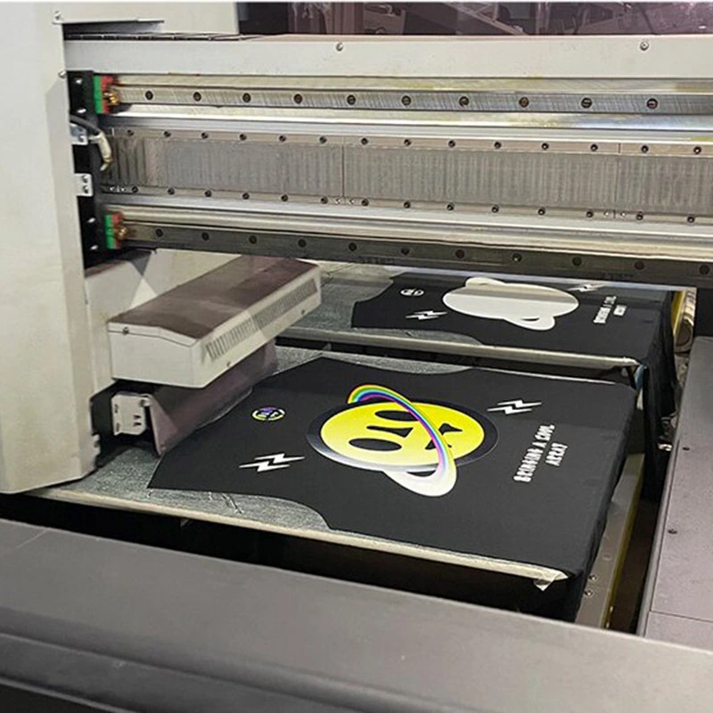 A garment printer applying a colored graphic to black T-shirts.