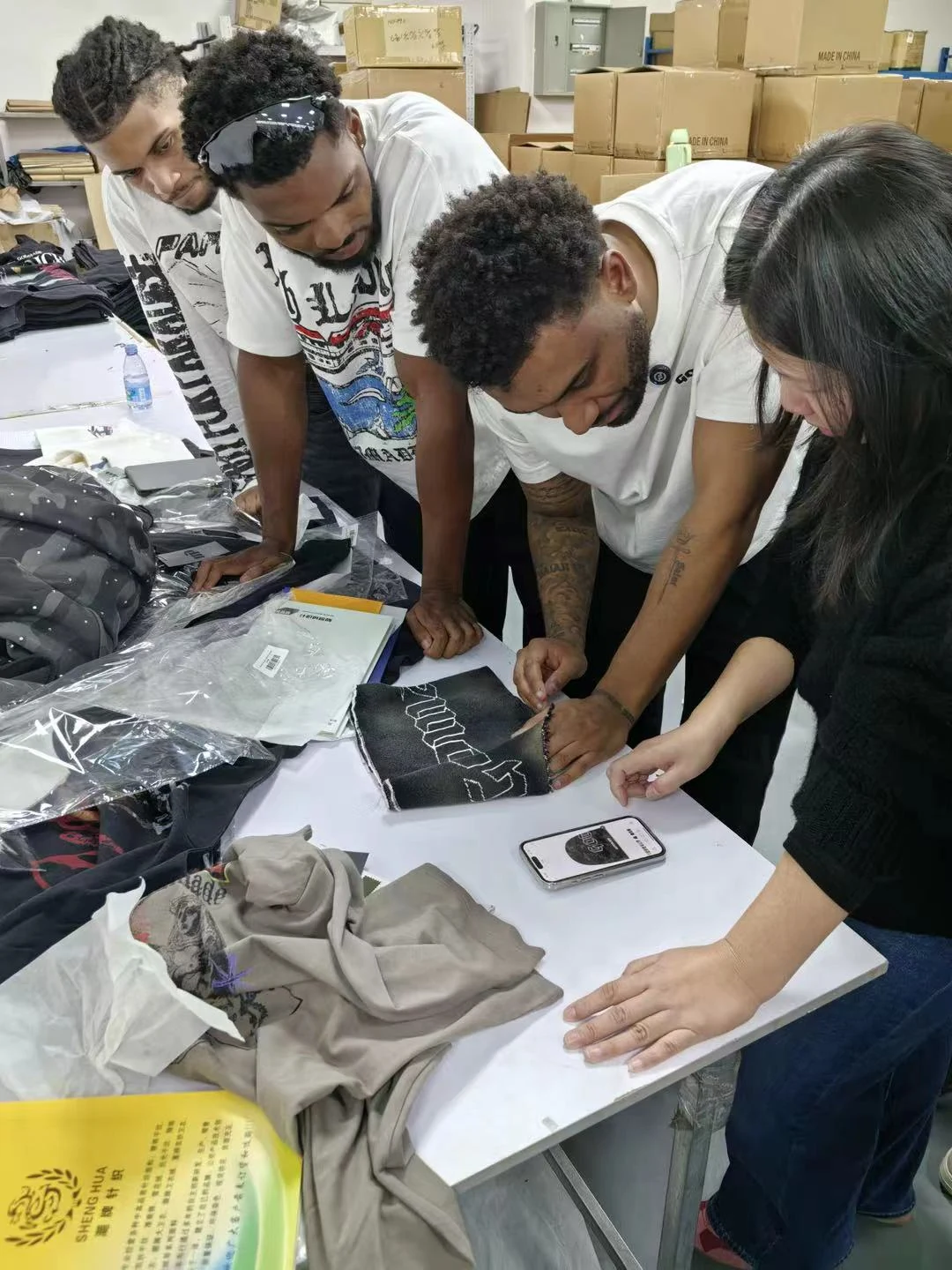 Customers and a SALATI team member examining a decorated garment panel alongside a phone reference